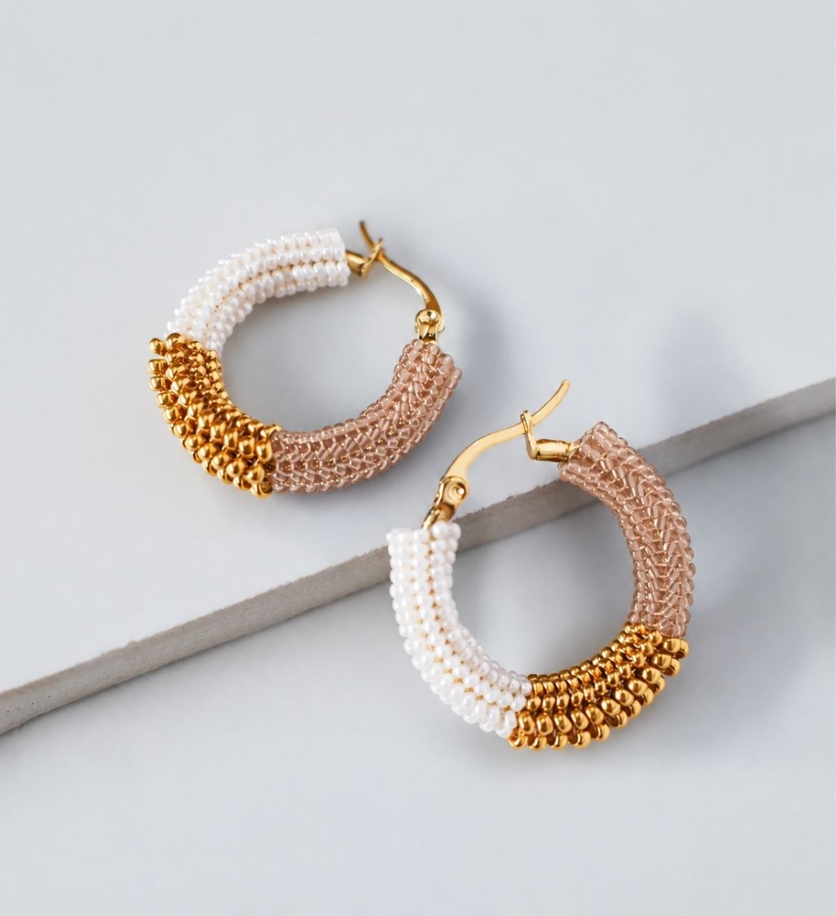 A pair of Eden & Elie handwoven gold and pink beaded hoop earrings
