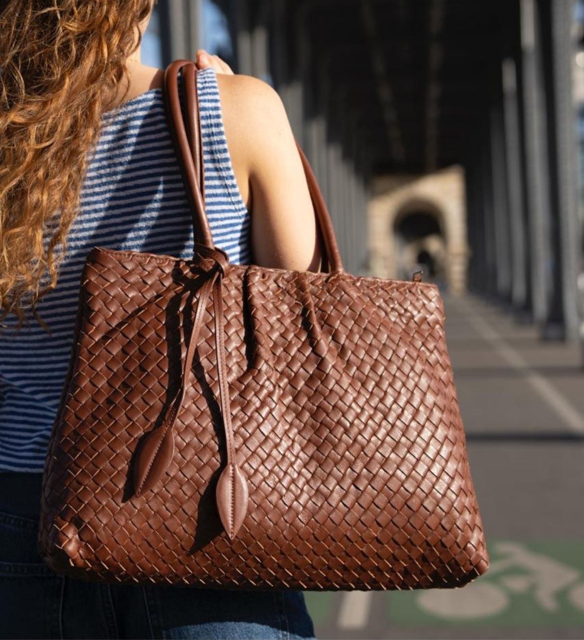 A woven brown leather tote bag carried over the shoulder
