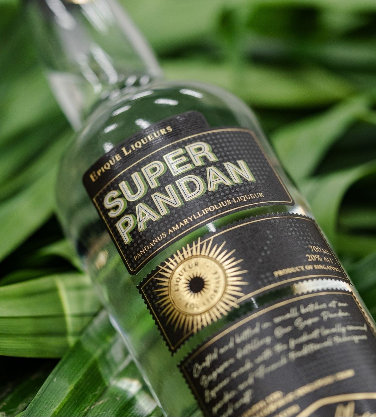 A bottle of Super Pandan liqueur resting on fresh pandan leaves